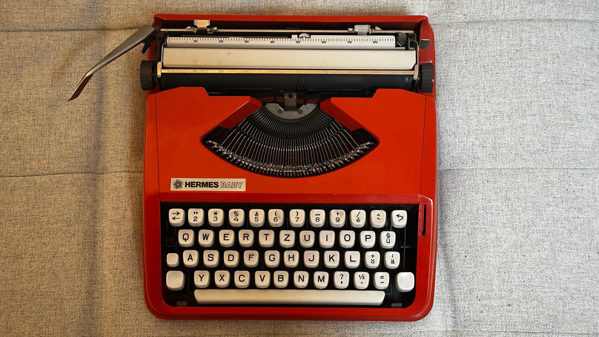Image of my orange Hermes Baby typewriter on my couch.