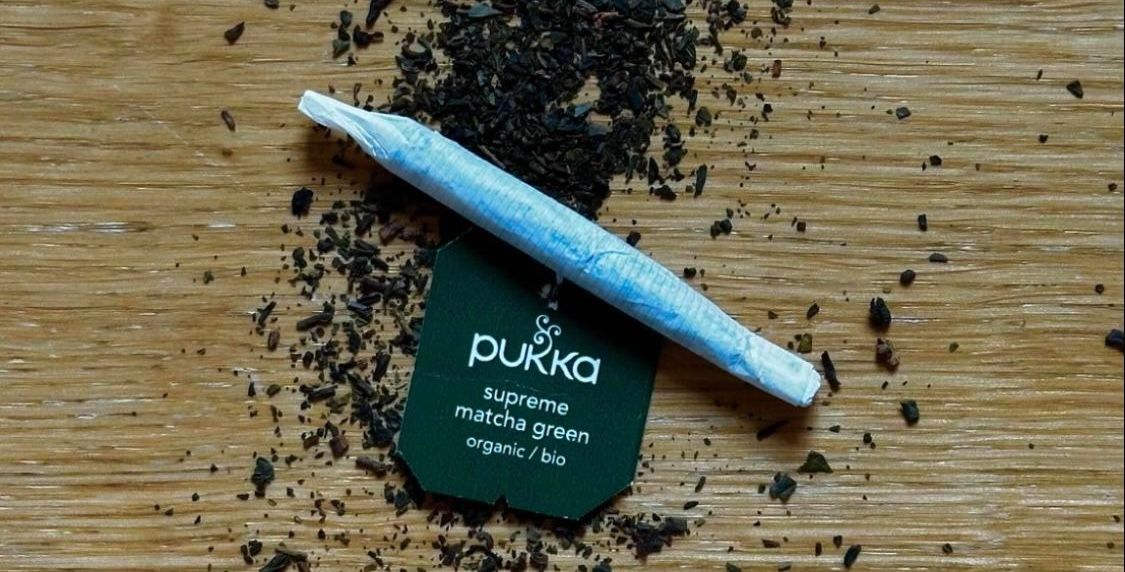 Photo of a rolled cigarette laid on green tea with the green tea label next to it reading "supreme matcha green".